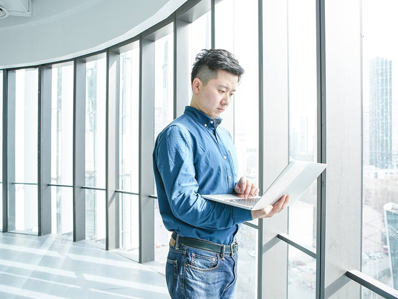 Man working on laptop standing near glass windows