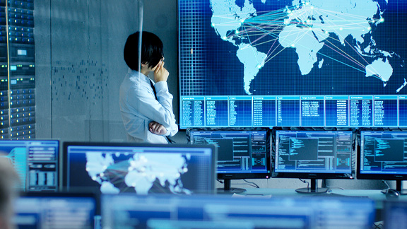 An employee is analyzing the feed from the computers on a big screen