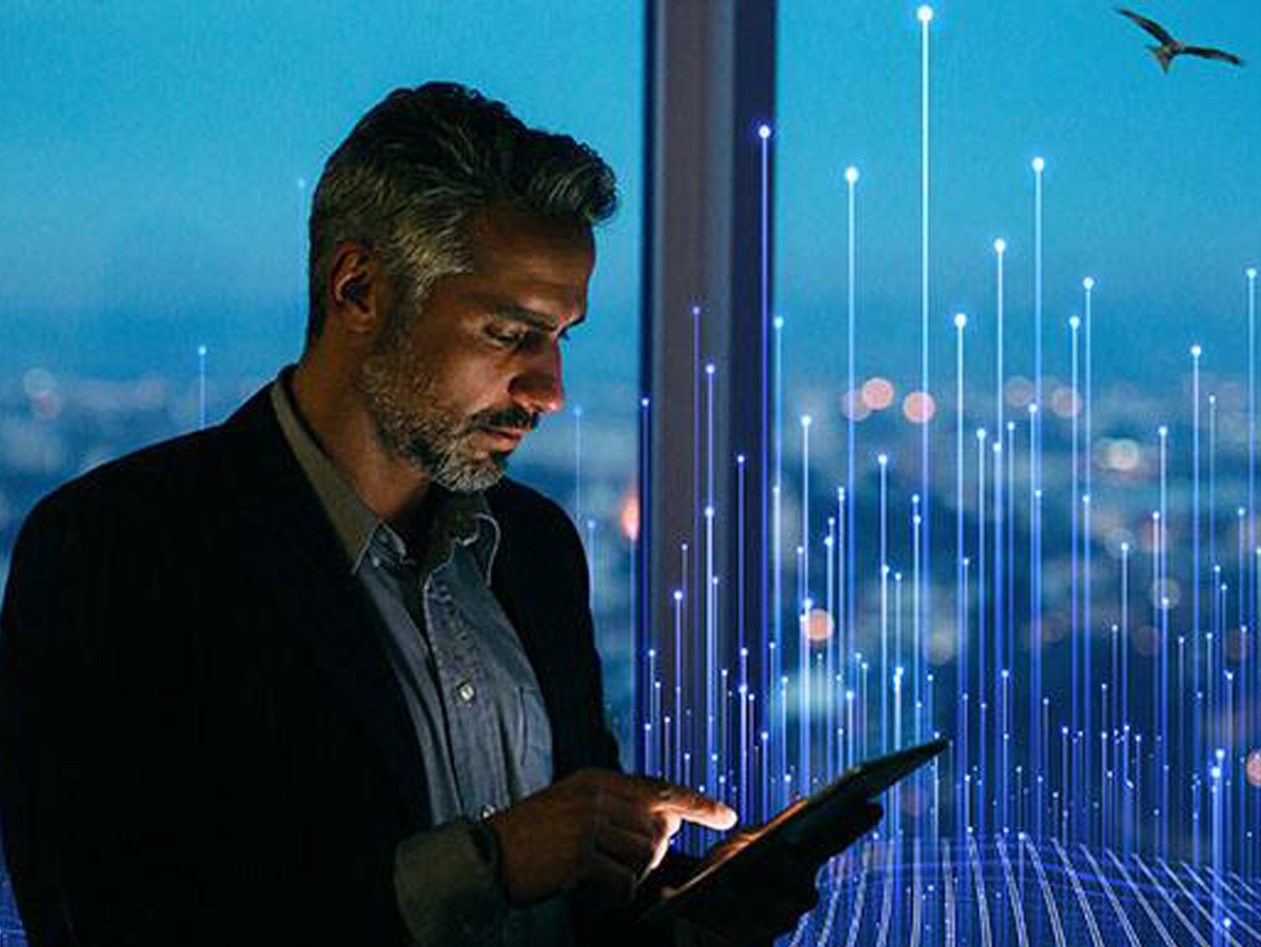 A man standing near the window and looking at a tablet in his hand overlaid with graphics of transmission nodes